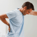 a man with back pain pressing his hand against the wall