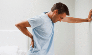 a man with back pain pressing his hand against the wall