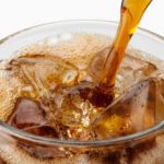 Soda being poured into glass with ice