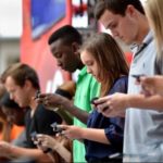 young people standing in the street looking at their mobile devices