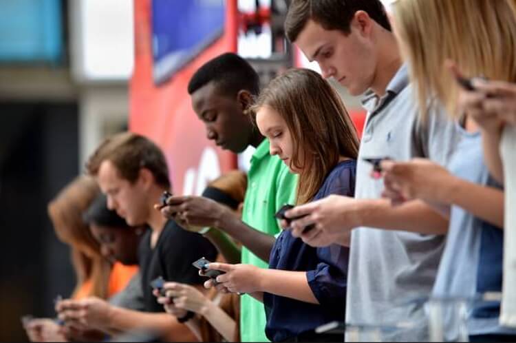young people standing in the street looking at their mobile devices