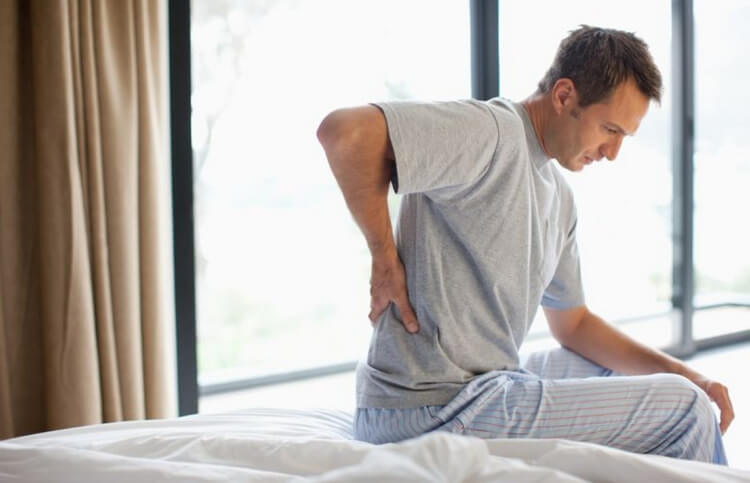 man with back pain sitting on his bed
