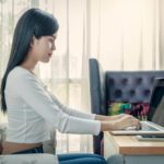 young woman sitting and writing on laptop